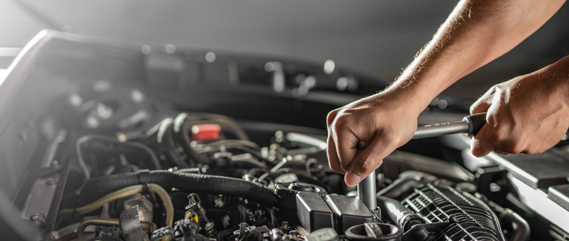 Un homme travaille sur un moteur de voiture avec une clé.