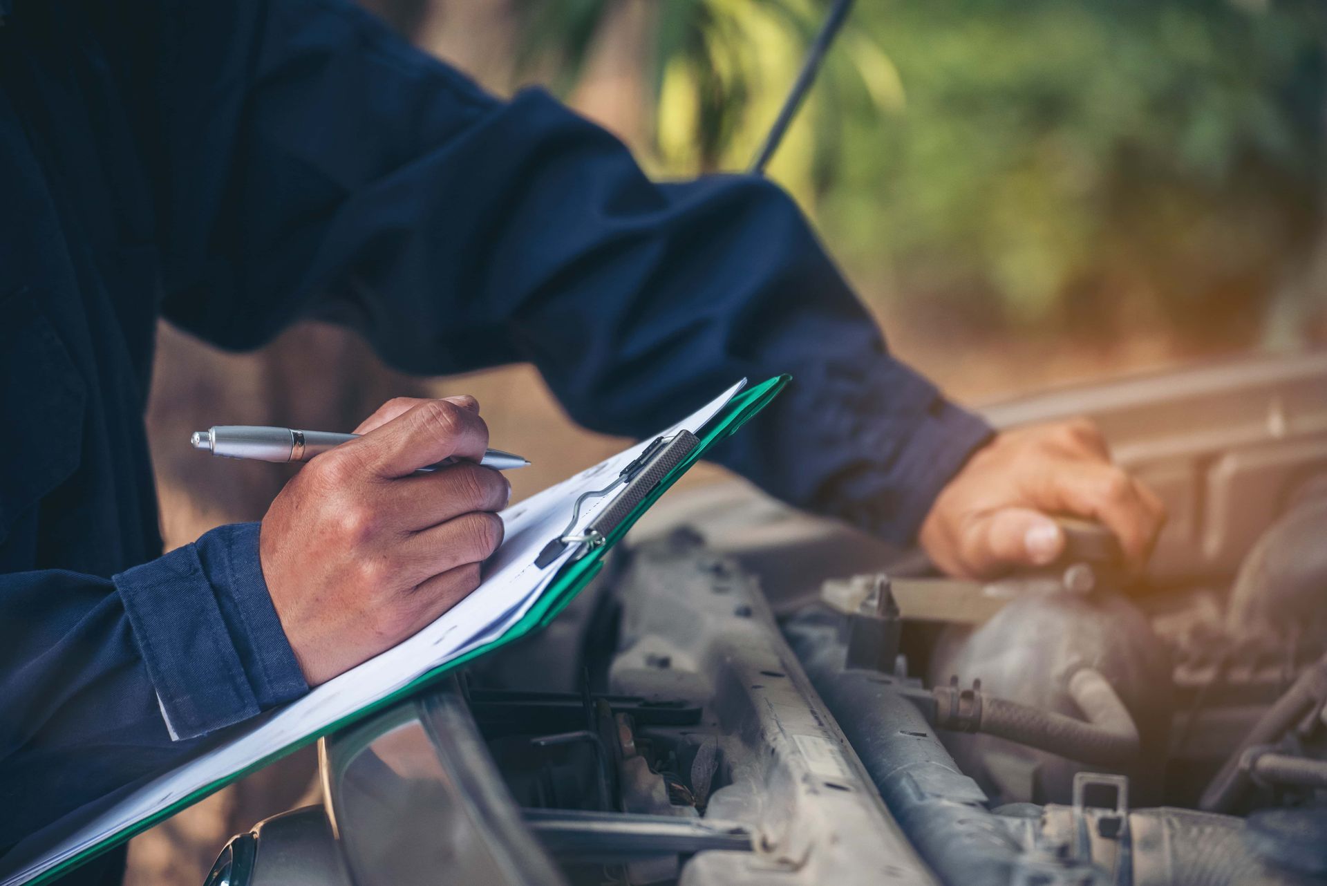 Un mécanicien écrit sur un presse-papiers tout en travaillant sur une voiture.
