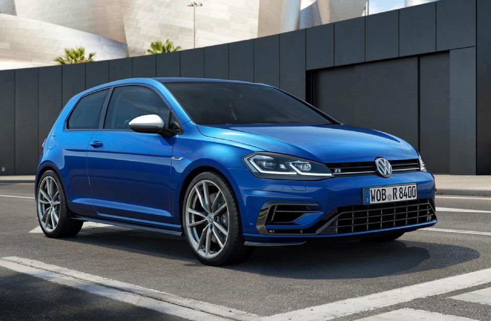 Une Volkswagen Golf R bleue est garée sur un parking devant un immeuble.