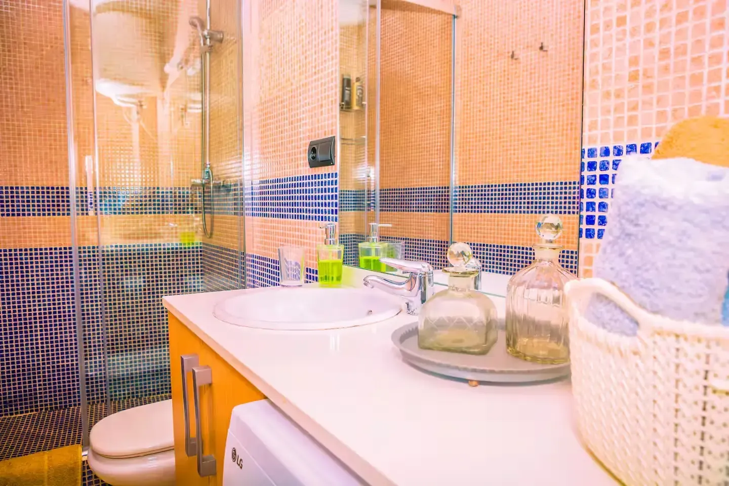 Baño con lavabo, espejo y azulejos azules y naranjas. Toallas en una cesta.
