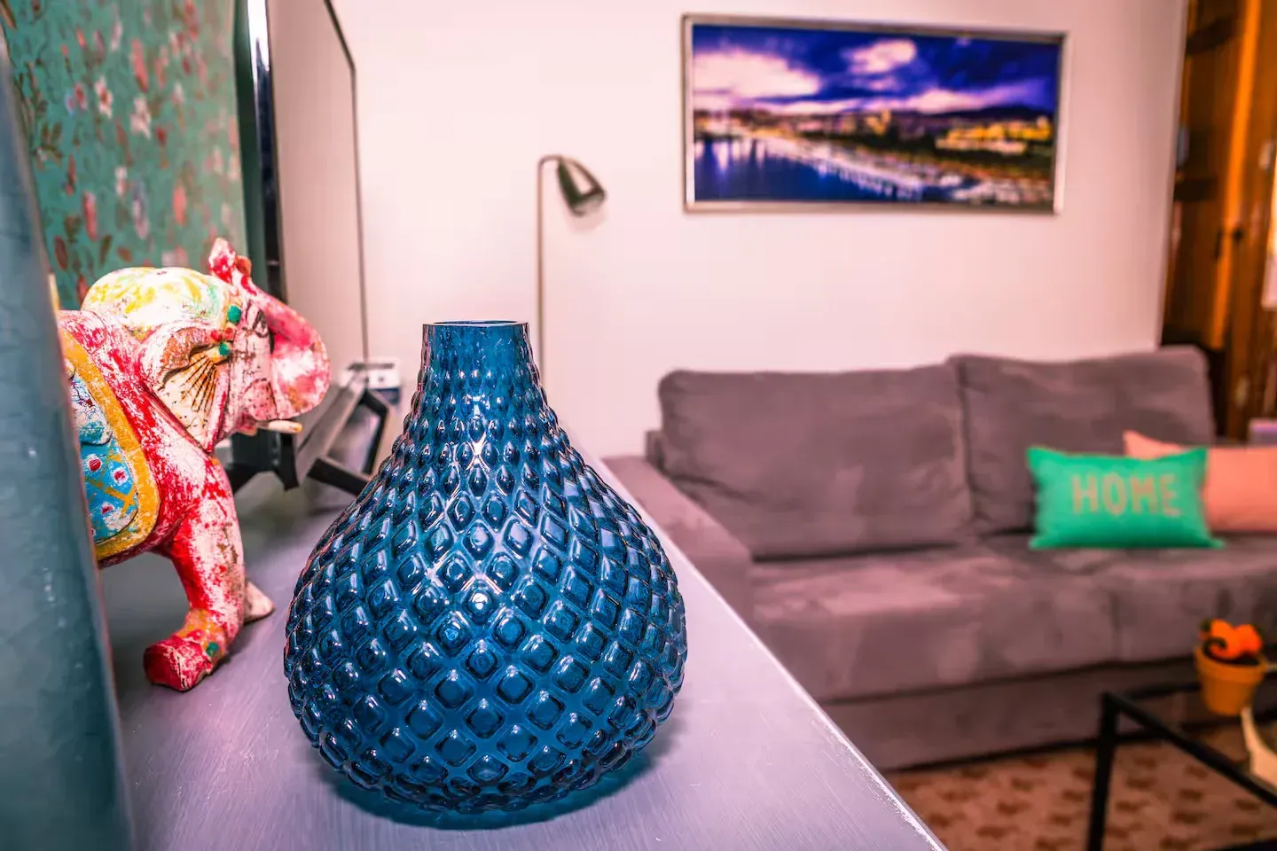 Jarrón azul y estatua de elefante en un estante; sofá gris en el fondo, arte en la pared.
