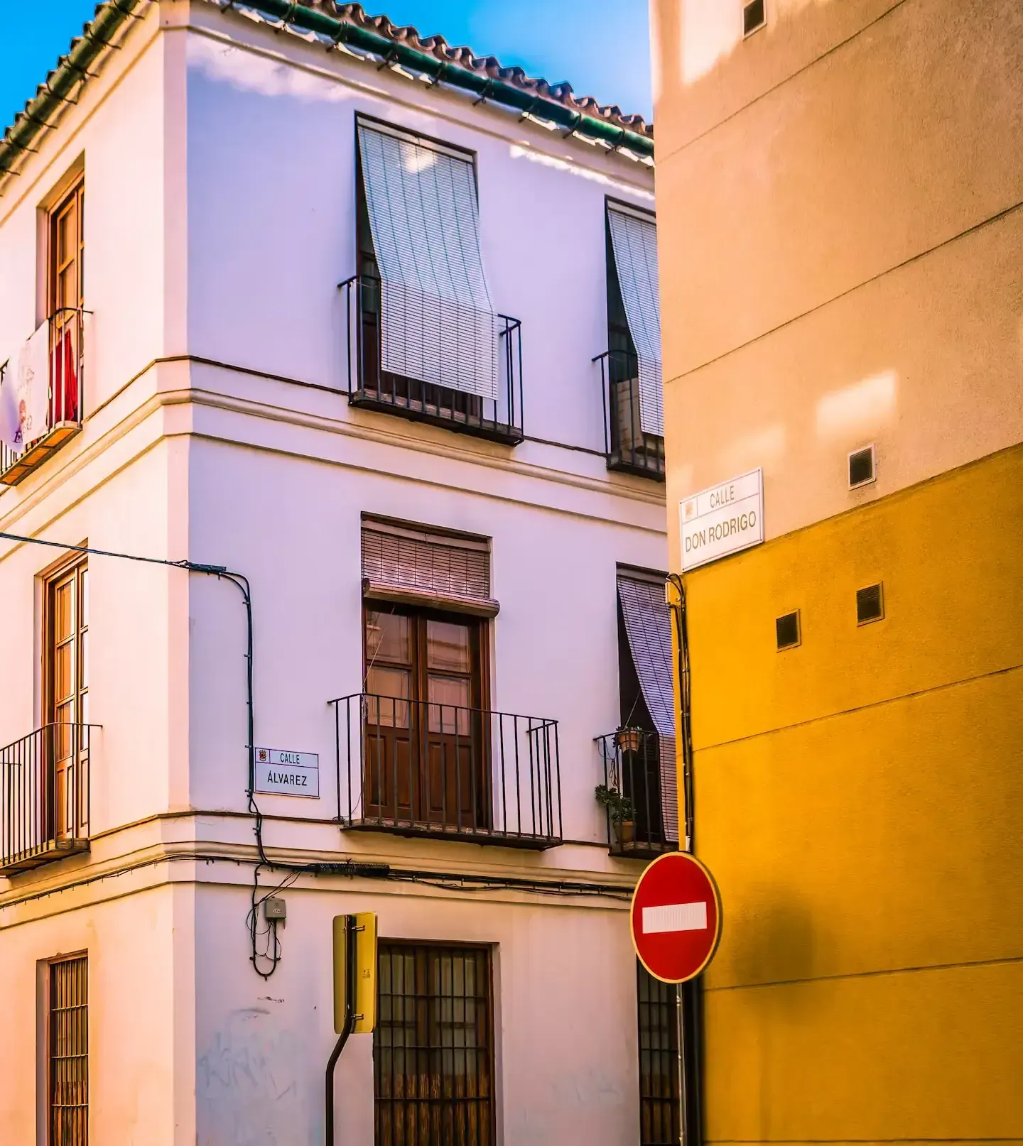 Edificio esquinero con fachadas blancas y amarillas, balcones y cartel de no entrar.