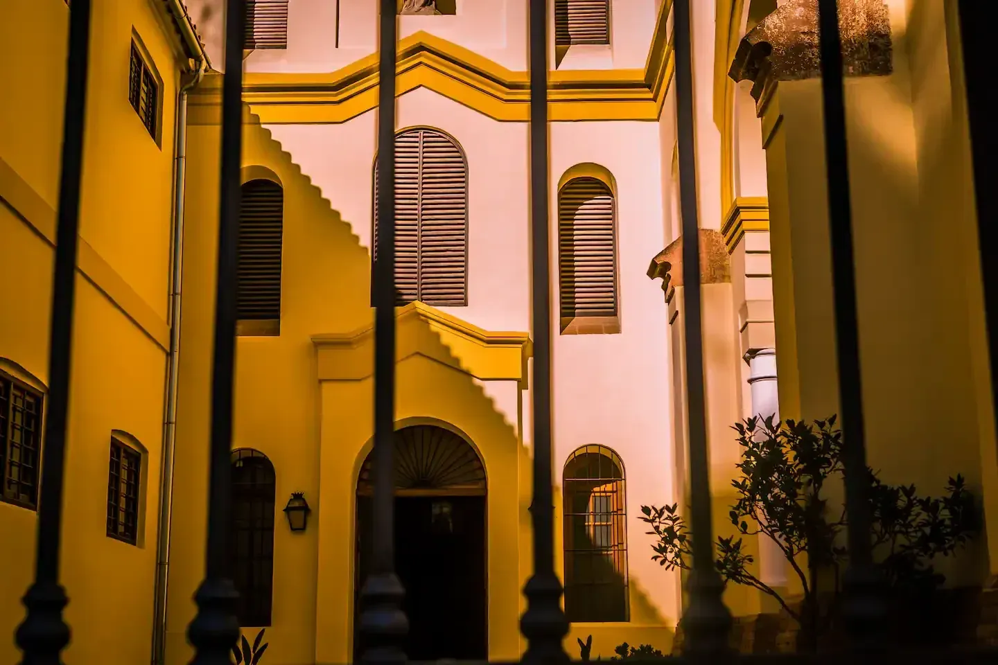Patio del edificio amarillo y blanco visto a través de barras verticales oscuras.