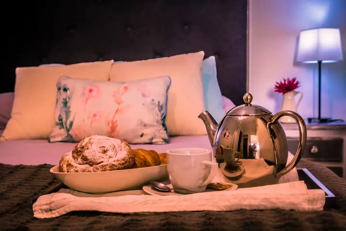 Bandeja de desayuno en la cama: pasteles, té y flores en un dormitorio.
