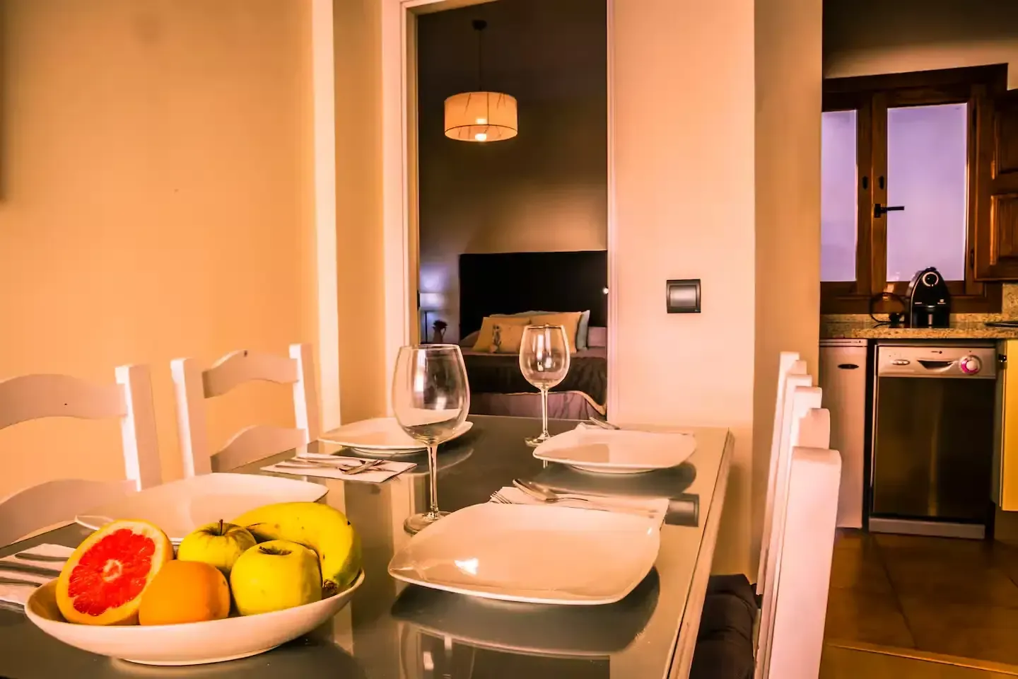 Comedor con frutero, mesa puesta para dos y vista al dormitorio y la cocina.