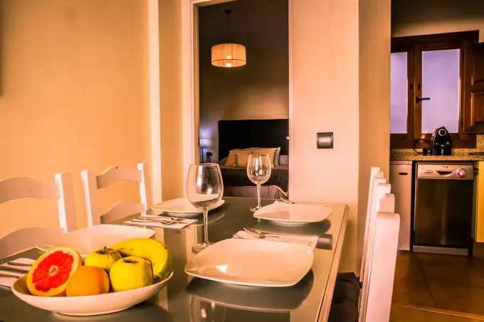 Comedor con frutero, mesa puesta para dos y vista al dormitorio y la cocina.