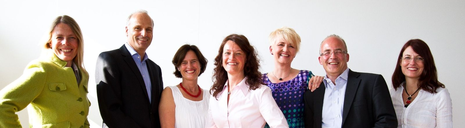 Eine Gruppe lächelnder Menschen steht vor einem weißen Hintergrund. 