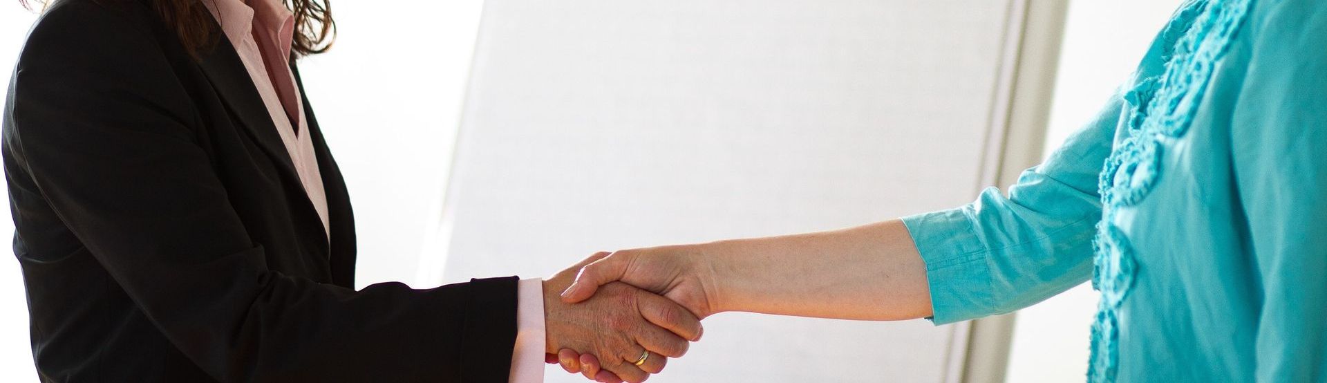 Zwei Personen schütteln sich die Hände vor weißem Hintergrund.