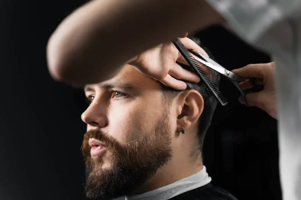 Un barbero corta el pelo a una clienta con tijeras y peine en un salón