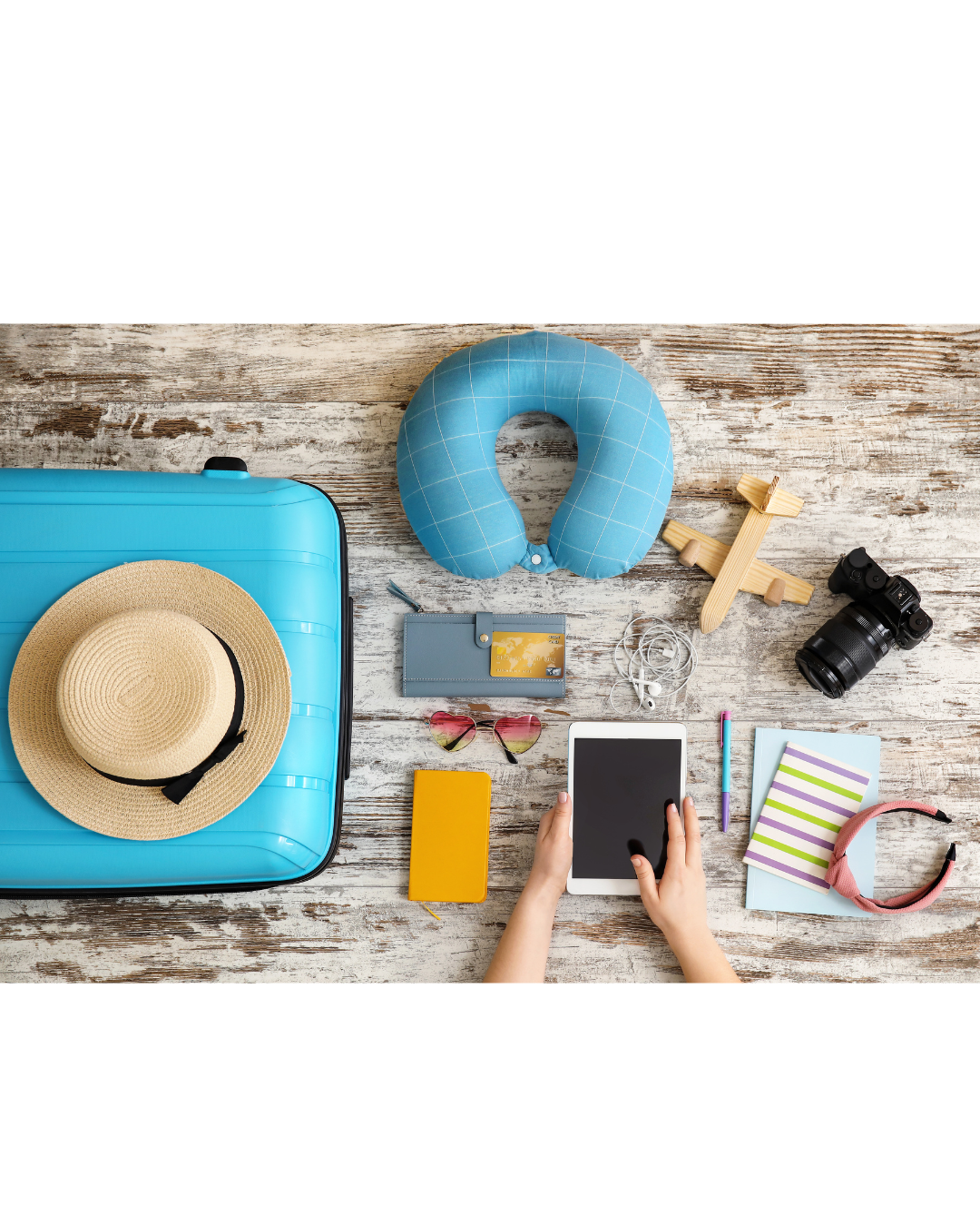 A person is using a tablet next to a suitcase and a hat.