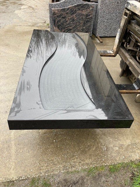 Pierre tombale en granit noir avec un design fluide sculpté.