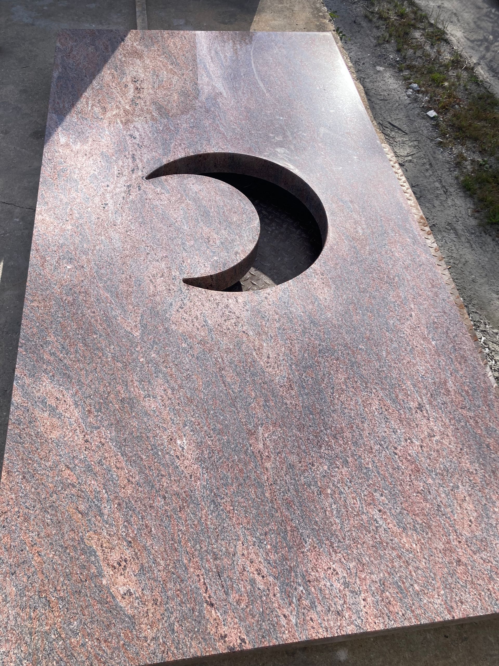Pierre tombale en granit rouge avec découpe en croissant de lune.