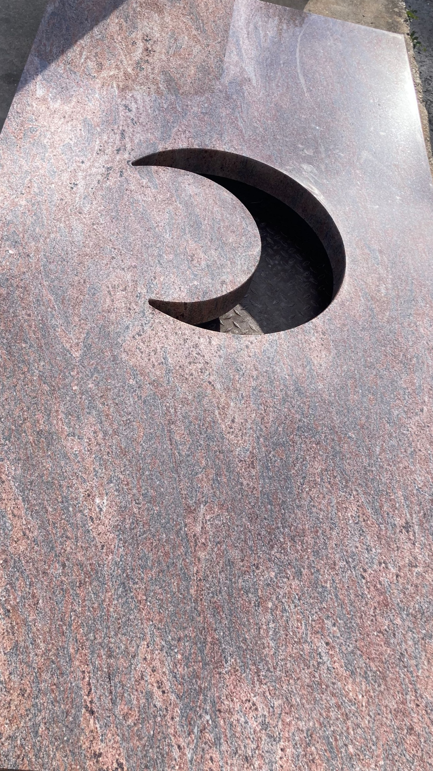 Une pierre tombale en granit rouge avec une découpe en forme de croissant.