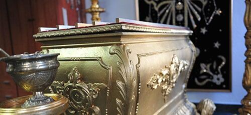 Um caixão de ouro está em uma igreja ao lado de um castiçal.