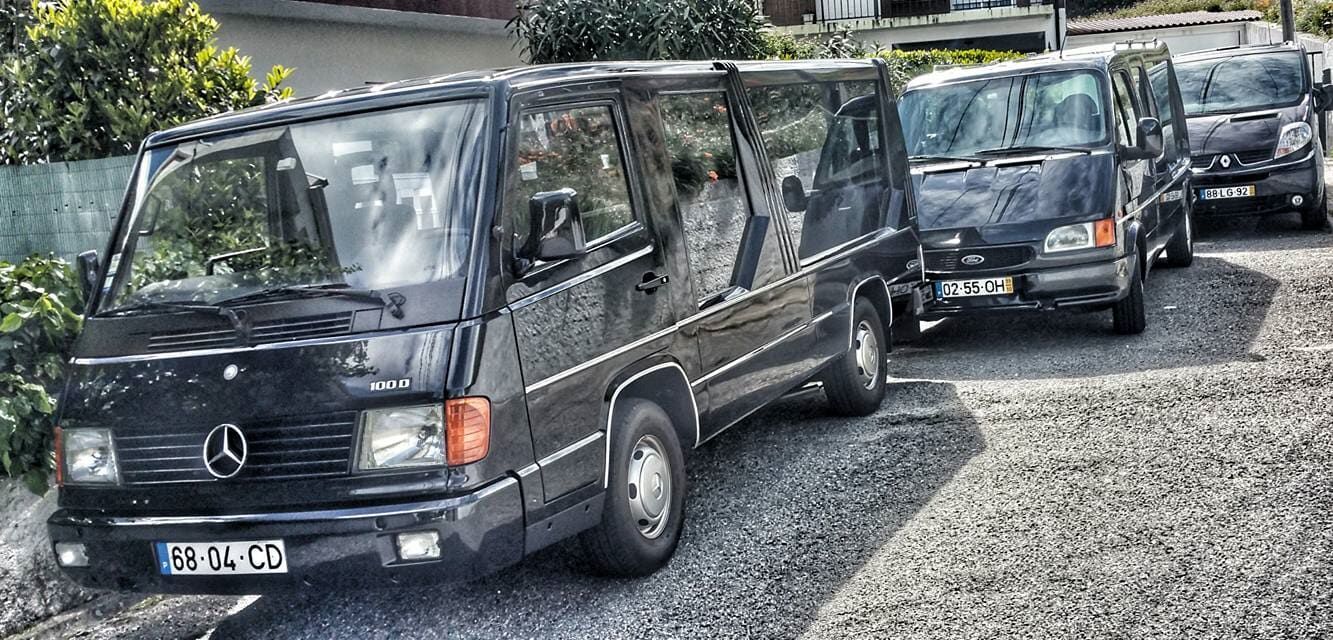 Uma fileira de vans Mercedes estão estacionadas em uma entrada de cascalho.