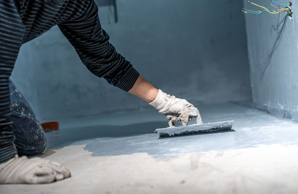 Handwerker trägt Abdichtungsmaterial auf dem Kellerboden auf, um Feuchtigkeit zu stoppen – Keller abdichten Firma St. Gallen.