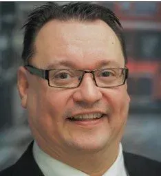 Silmälasipäinen, hymyilevä, puvussa oleva mies, kasvokuva.