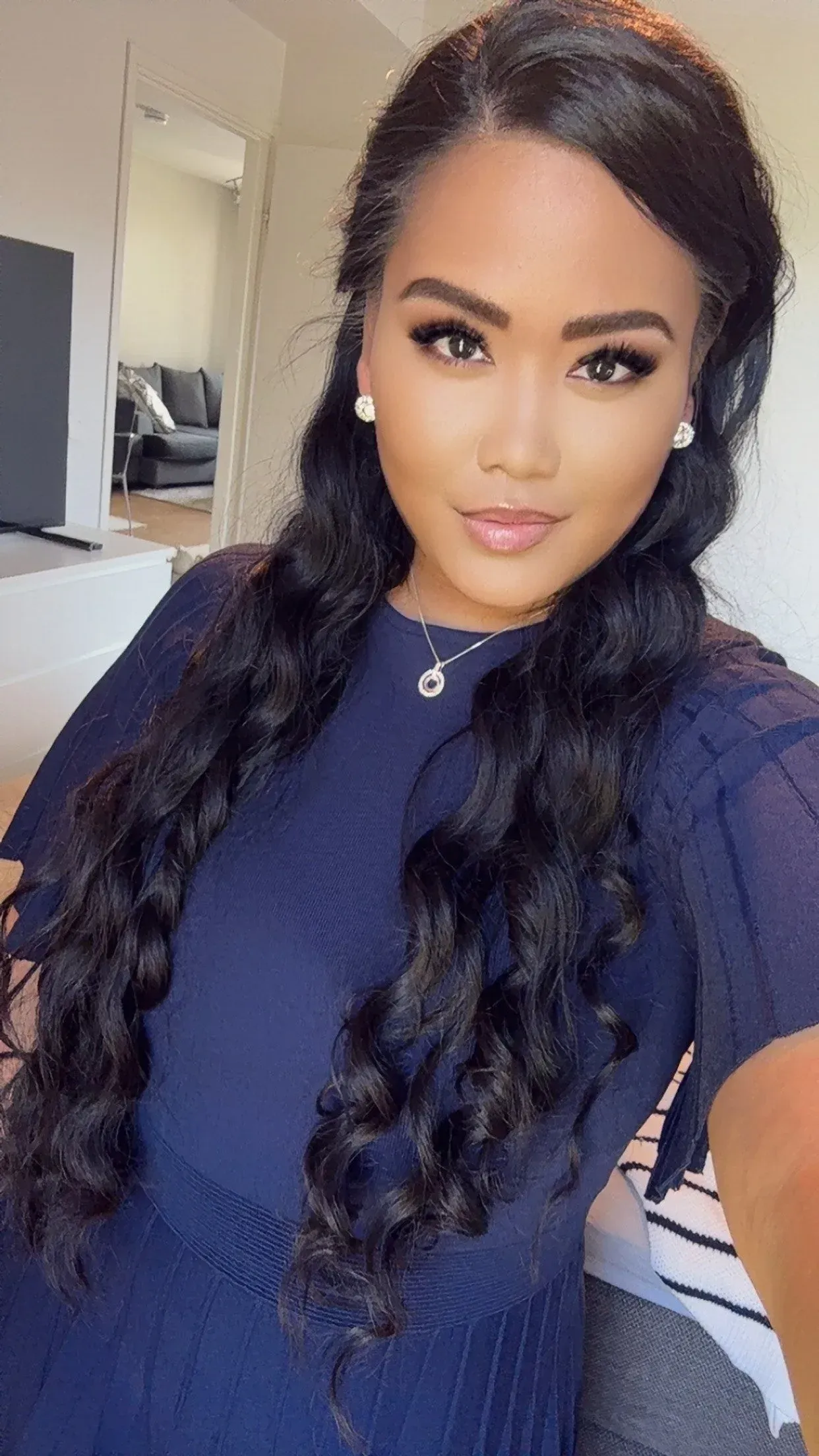 Nainen, jolla on pitkät, laineikkaat mustat hiukset ja sininen mekko, katsoo kameraan.