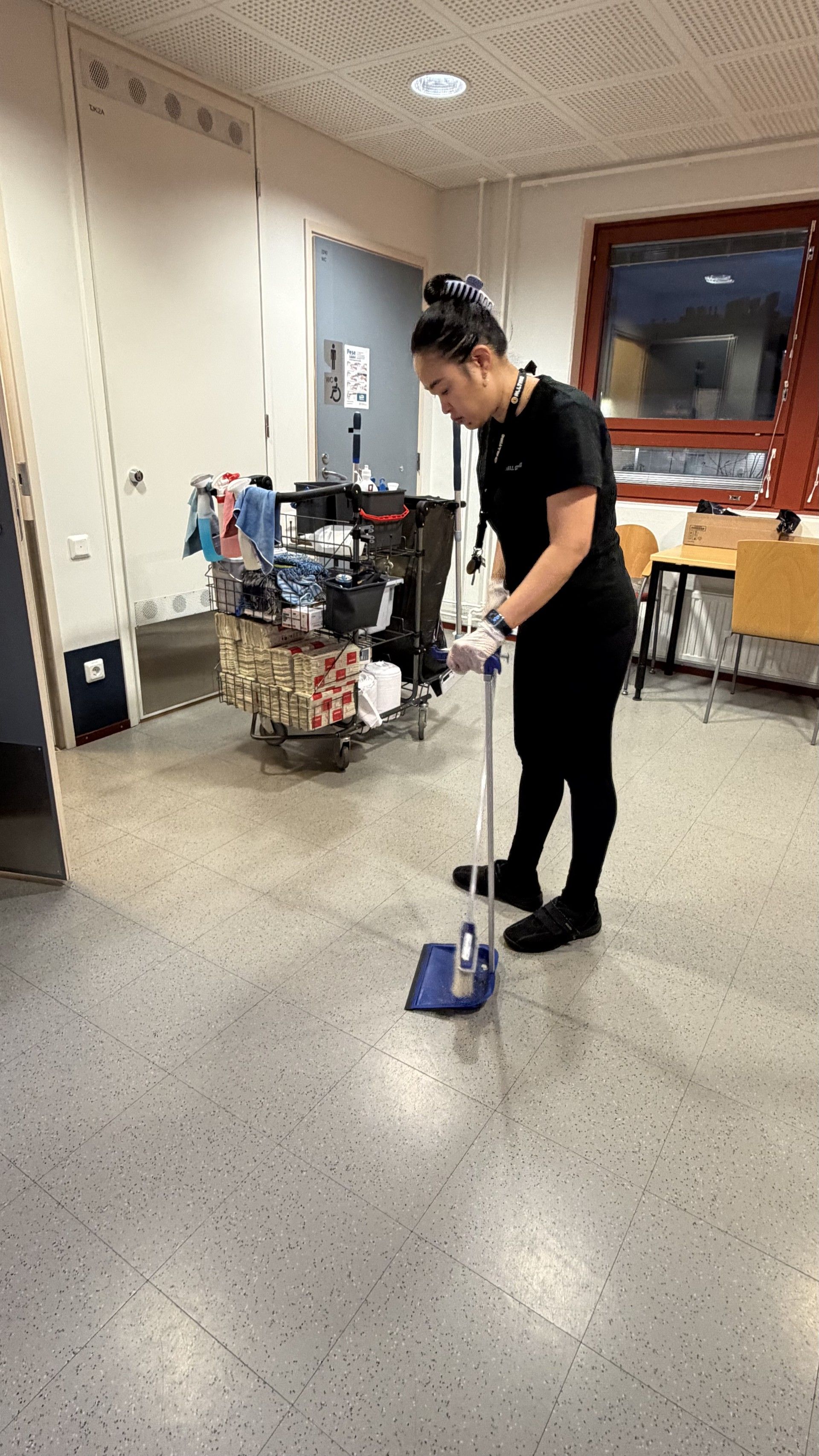 Henkilö moppaa harmaata lattiaa huoneessa. Siivousvälinekärry näkyvissä.