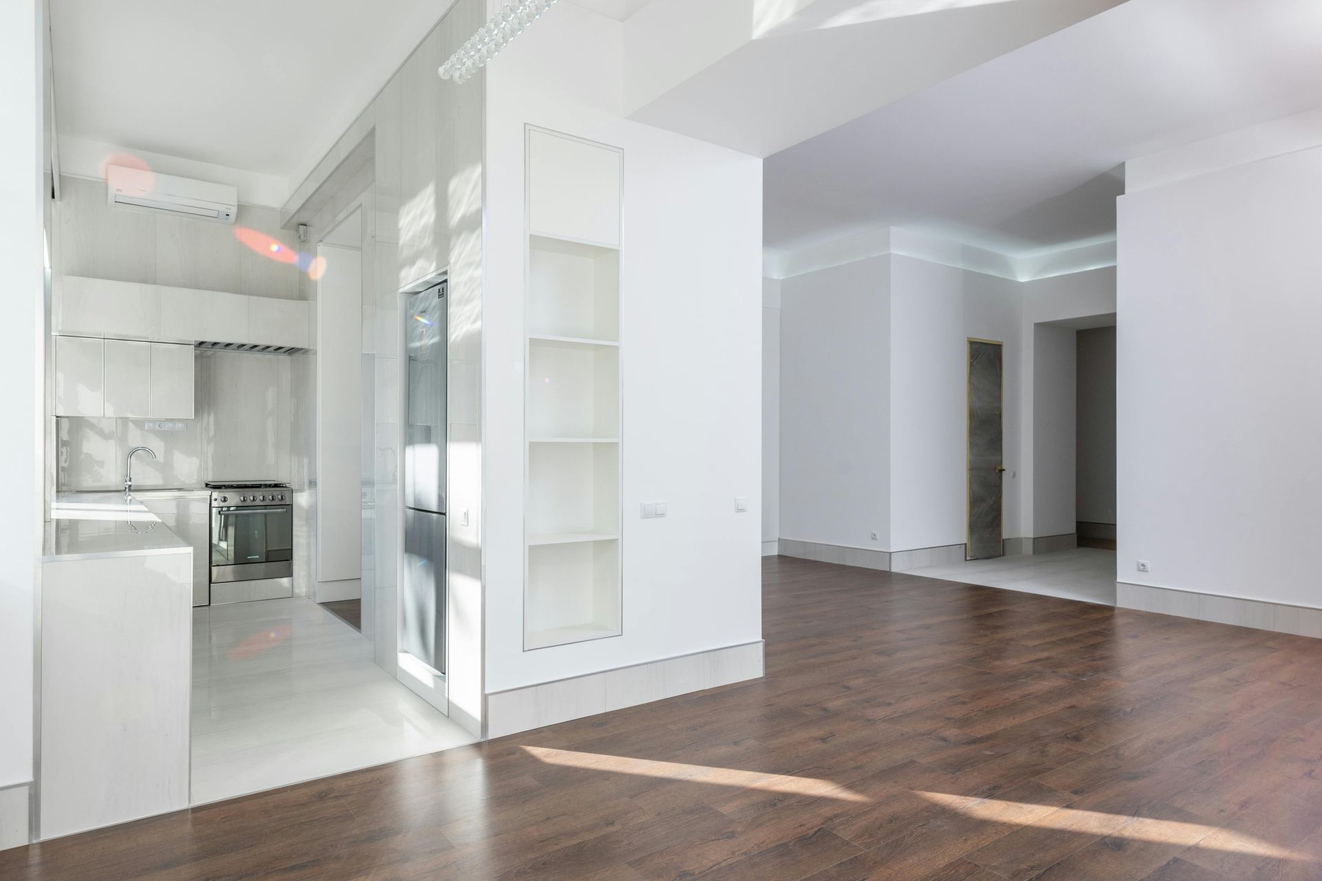Moderni, tyhjä valkoinen asunnon sisustus, jossa tummat puulattiat. Keittiö vasemmalla, avoimet oviaukot oikealla.