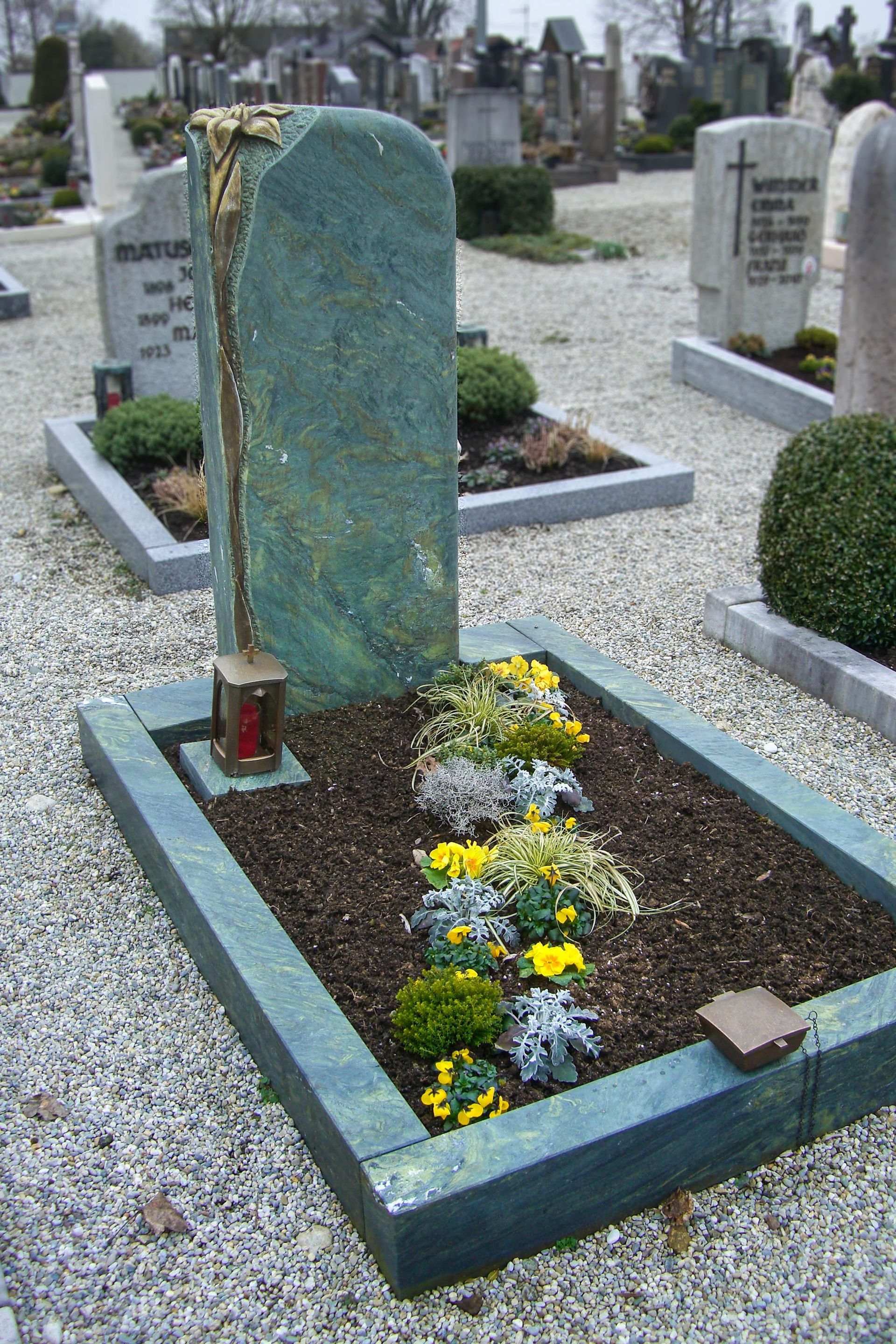 ein grüner Grabstein in einem Friedhof mit Blumen und Kerzen