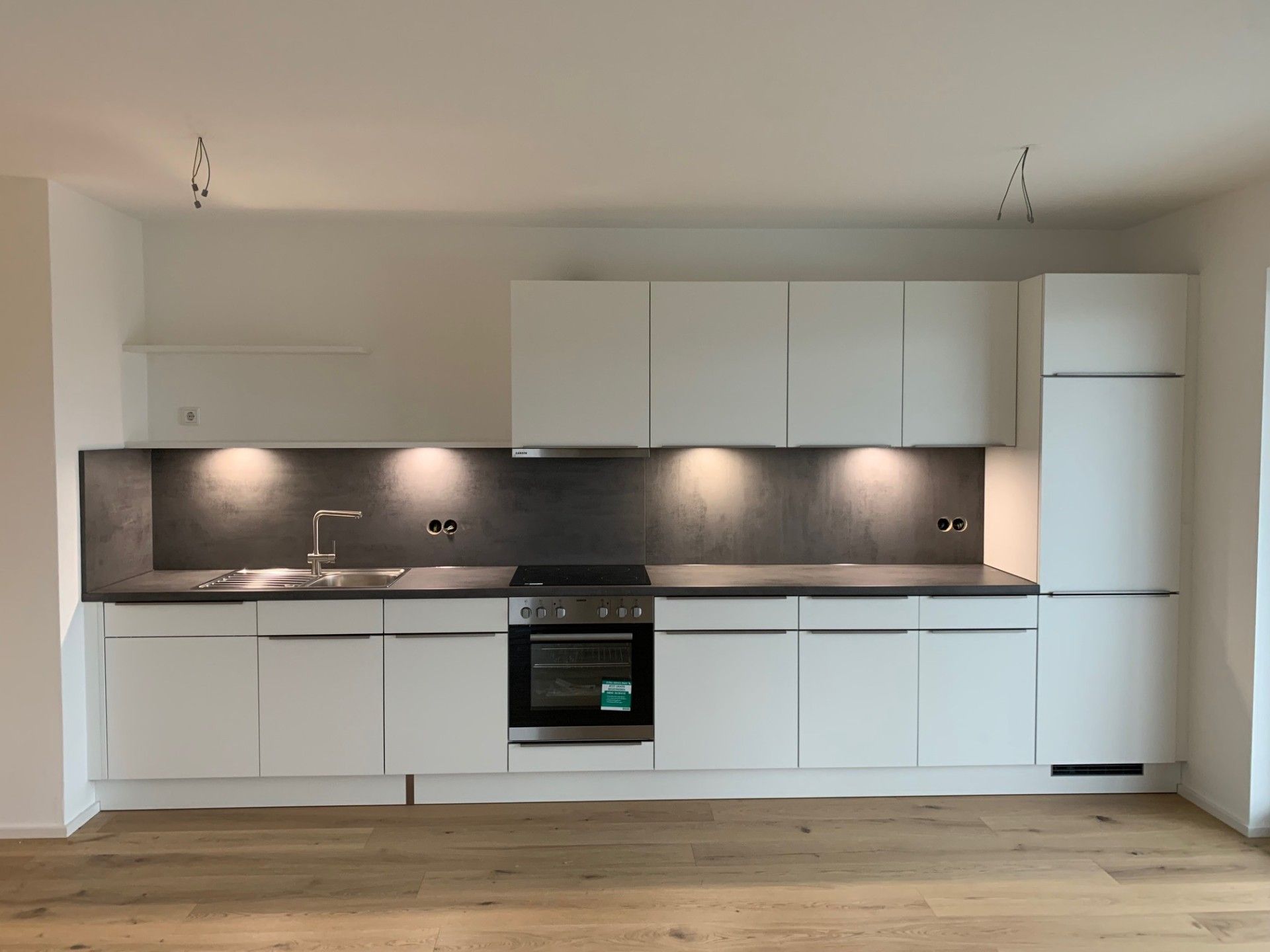Moderne weiße Küche mit schwarzem Fliesenspiegel, Einbaubackofen und hellem Holzboden