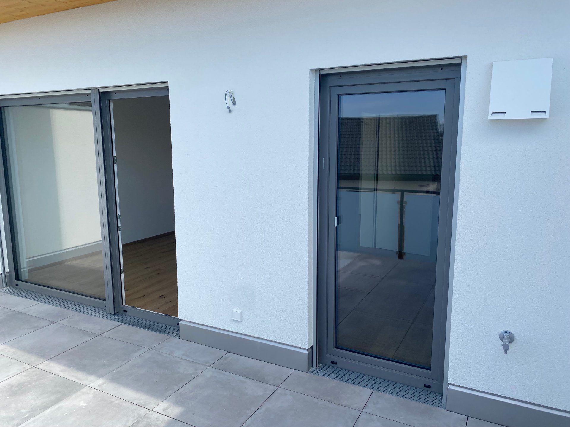 Wohnungsterrasse mit Glasschiebetür, dunkelgrauer Eingangstür und weißer Außenwand