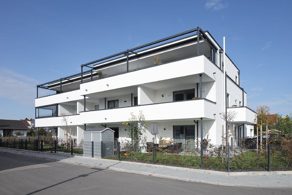 Modernes weißes Mehrfamilienhaus mit Balkonen und Dachterrasse in einer ruhigen Straße