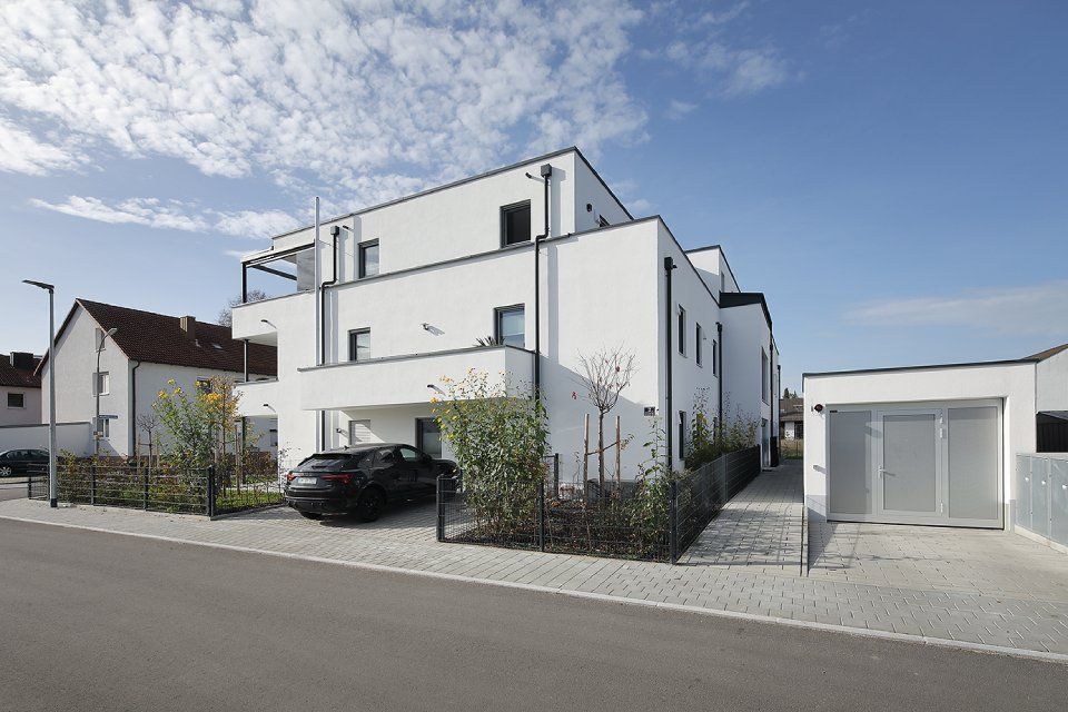 Modernes weißes Wohnhaus mit Carport, Einfahrt und freistehender Garage unter blauem Himmel