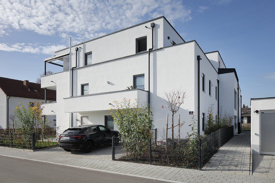 Modernes, weißes zweistöckiges Haus mit Carport, schwarzem Auto und umzäuntem Vorgarten