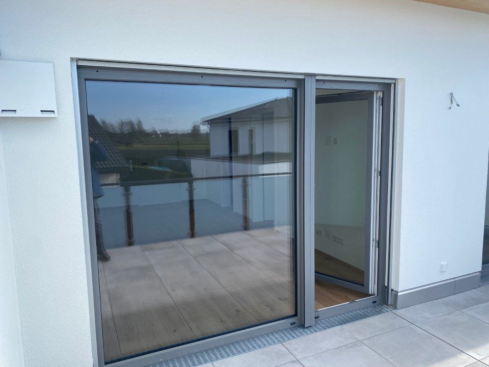 Schiebetüren aus Glas führen auf einen Balkon mit Glasgeländer und Fliesenboden.