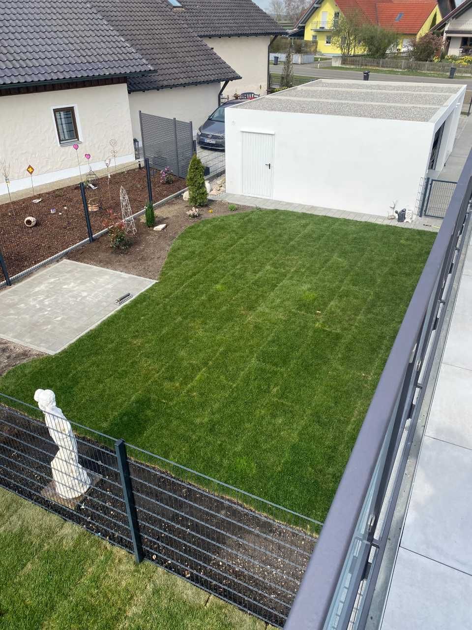 Hinterhof mit grünem Rasen, weißem Schuppen, schwarzem Zaun und den Nachbarhäusern aus der Vogelperspektive