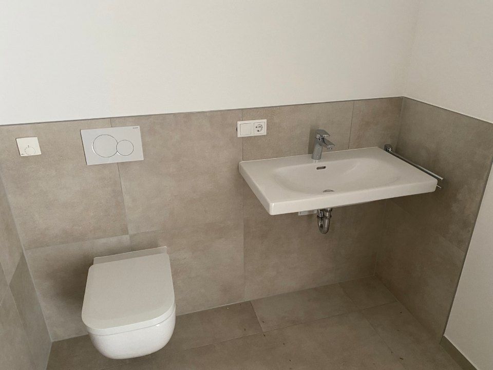 Barrierefreie Toilette mit wandhängendem WC, Waschbecken und beigefarbenen Fliesenwänden
