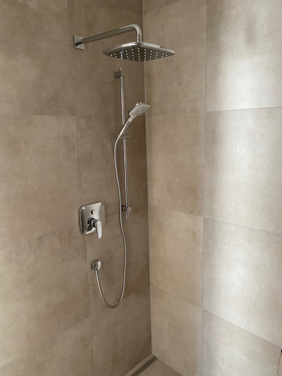 Moderne Dusche mit verchromtem Duschkopf und Handbrause vor beigefarbenen Fliesenwänden