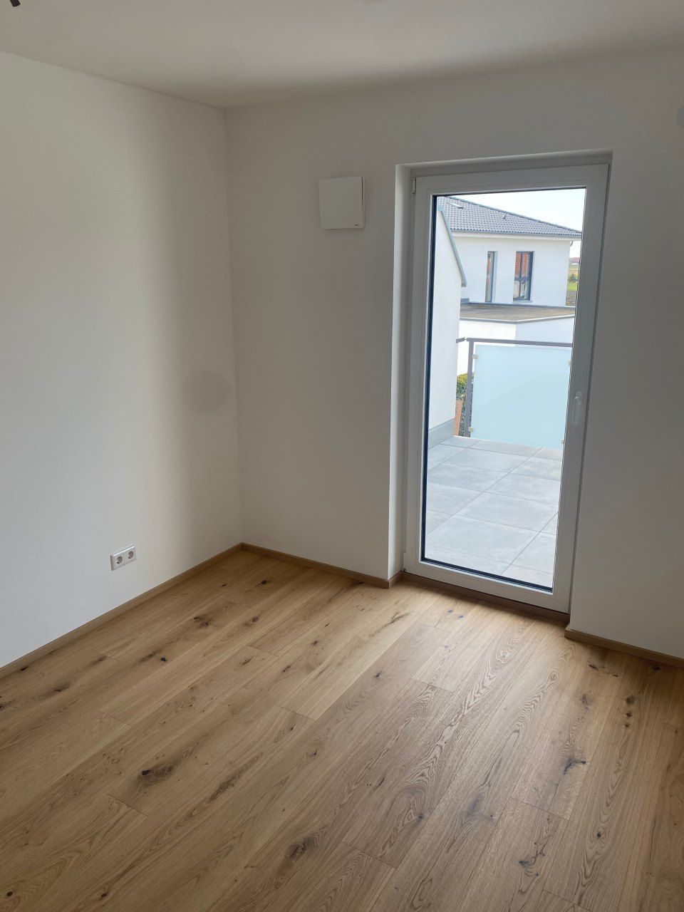 Leerer Raum mit Holzboden und einer Glastür, die zu einem Innenhof führt.