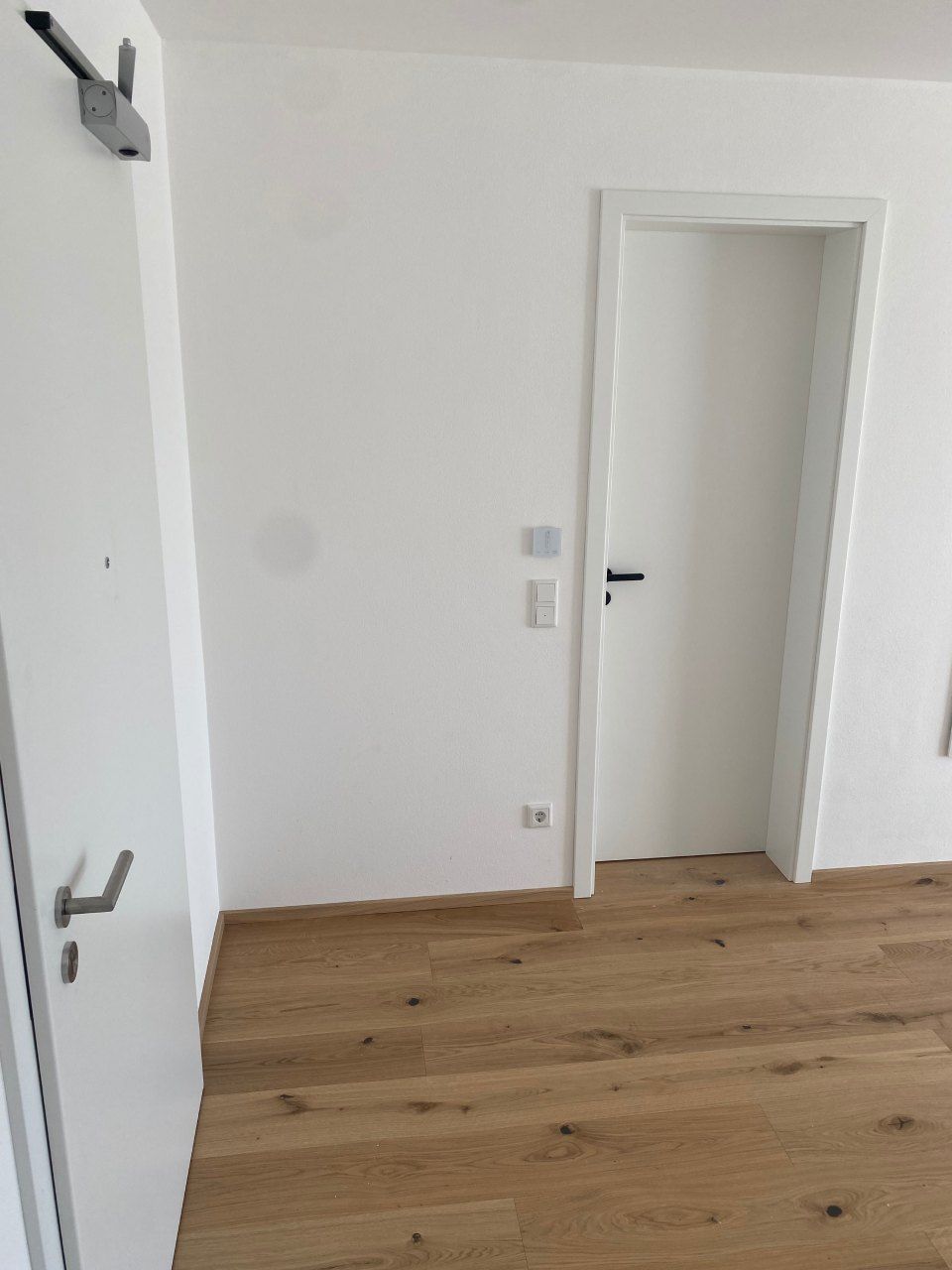 Leerer weißer Raum mit Holzboden und offener Tür zu einem Flur