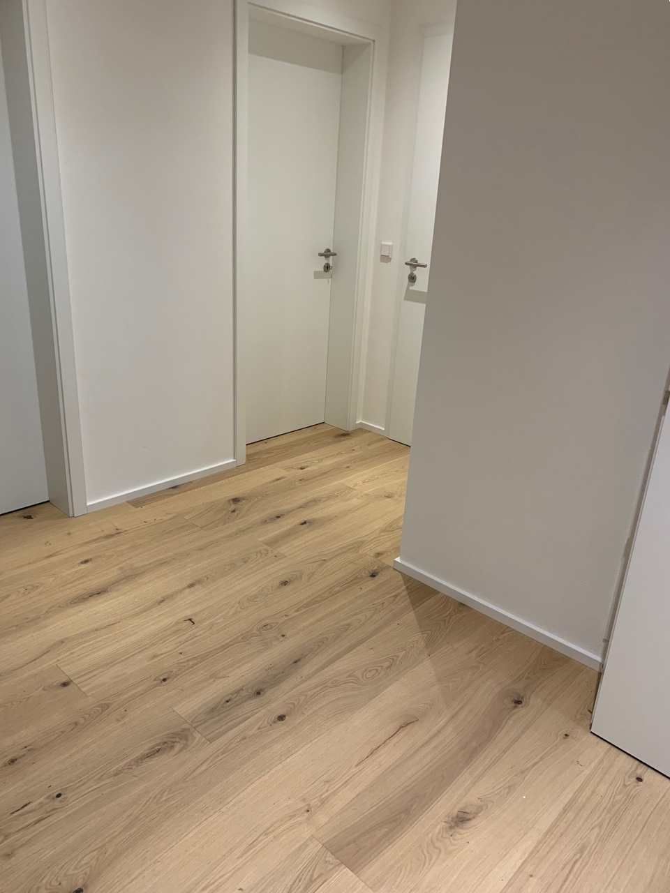 Leerer Flur mit hellem Holzboden und weißen Türen, von einer Ecke aus betrachtet.