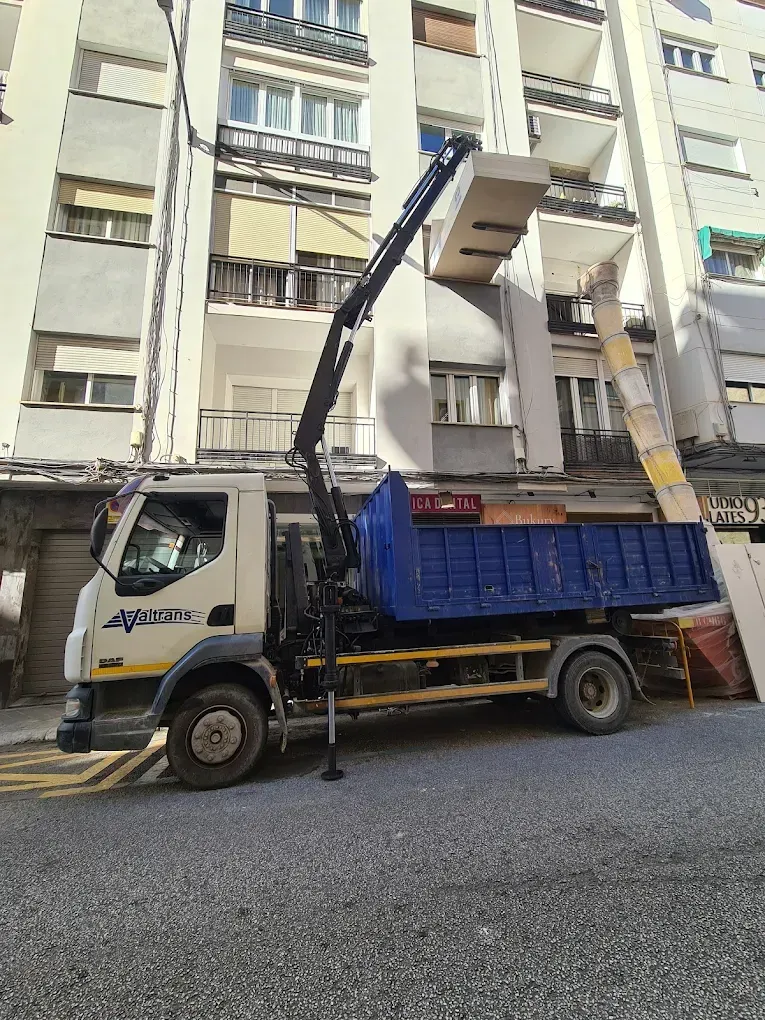 Camión con grúa levantando un artículo rectangular de gran tamaño hacia un edificio de apartamentos.