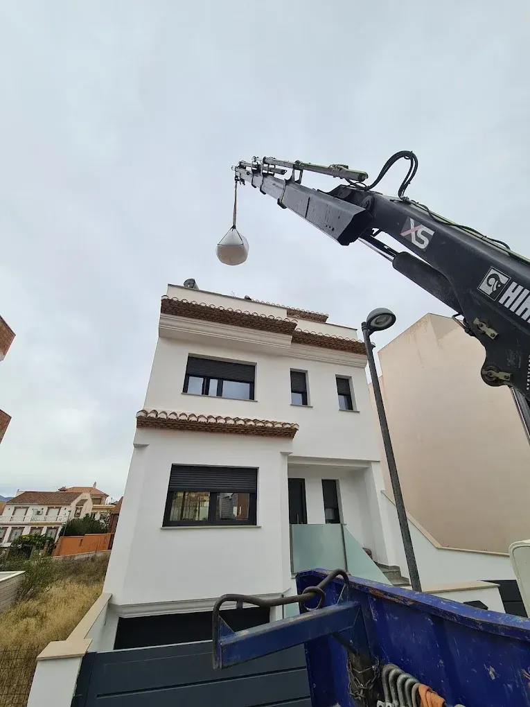 Dos imágenes: un trabajador en una escalera alta pintando una pared exterior y un trabajador en un andamio enyesando un techo.