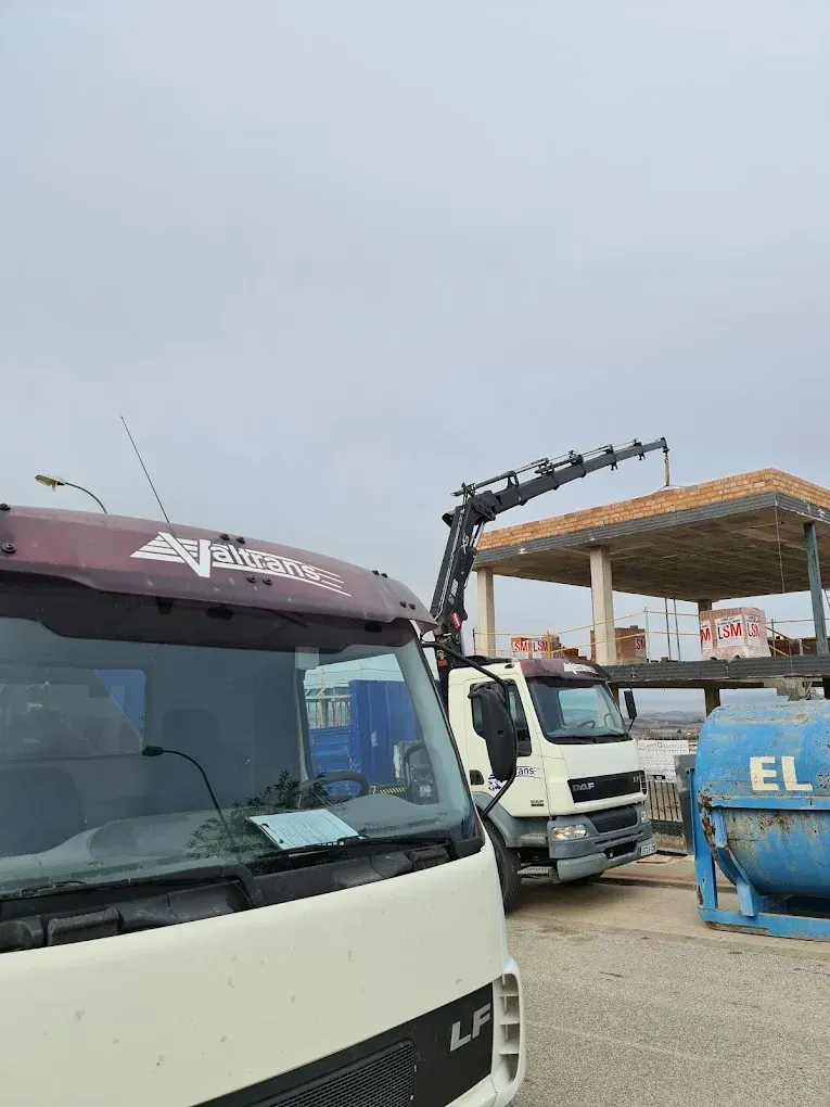 Obra con camión grúa. Se ve una hormigonera en primer plano con otro camión.