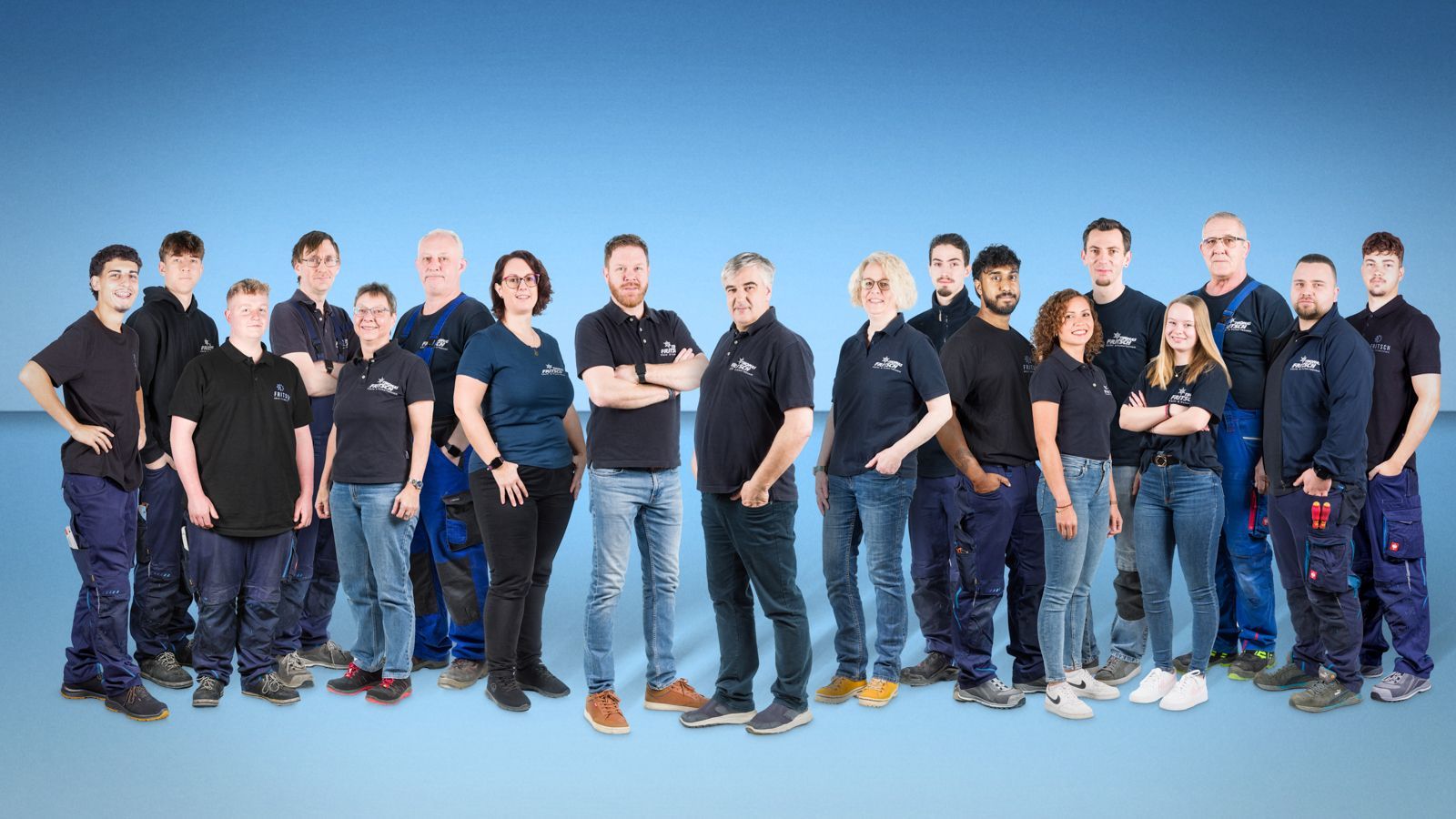 Gruppe von Menschen in schwarzen oder dunkelblauen Hemden und Jeans, die vor einem blauen Hintergrund stehen.