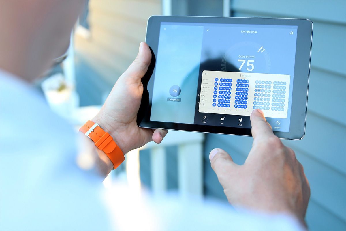 Person stellt im Freien einen Thermostat auf einem Tablet ein. Zeigt 75 Grad an, blaue Hausverkleidung.