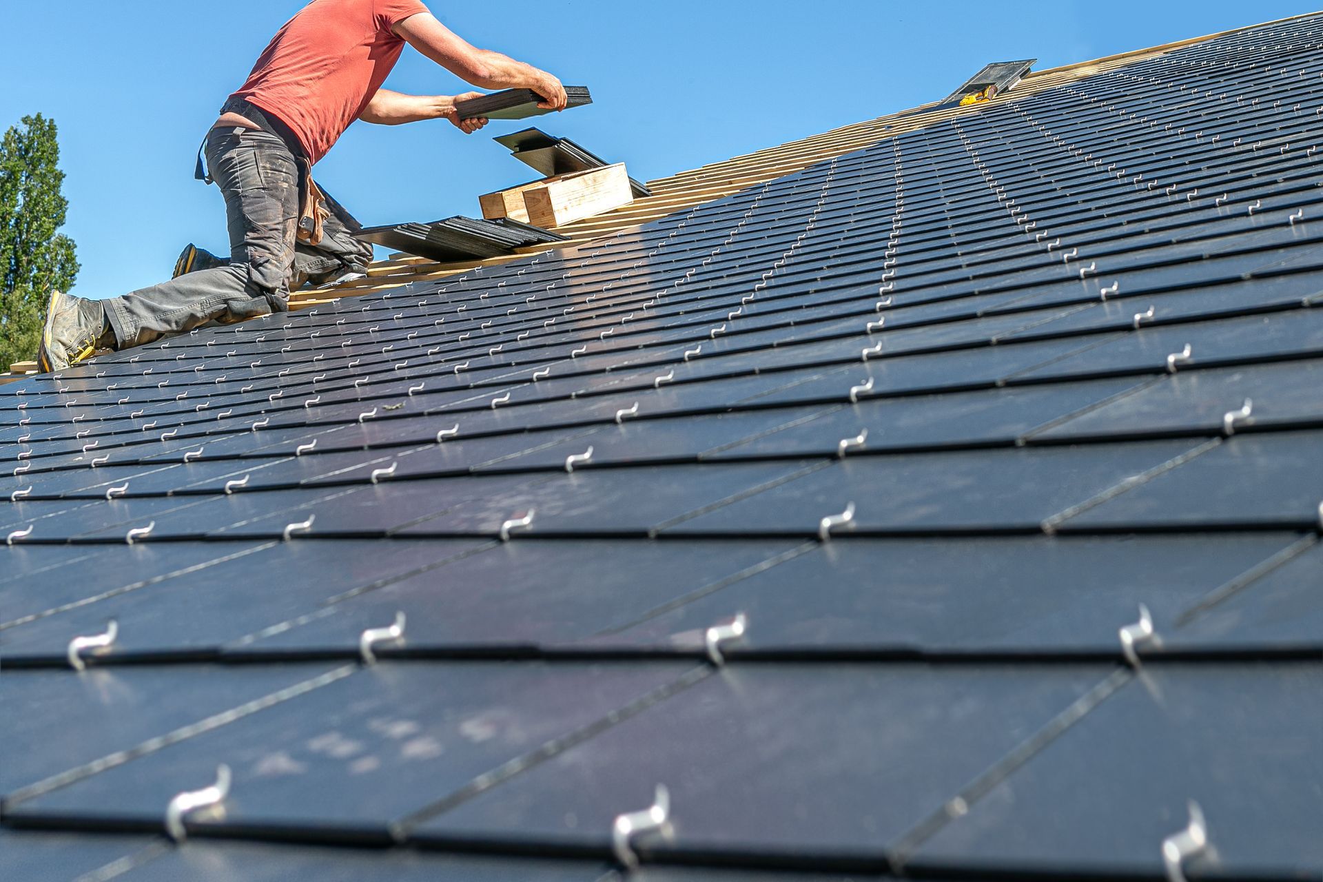 Un couvreur pose des tuiles solaires gris foncé sur une maison. Ciel d'un bleu éclatant.