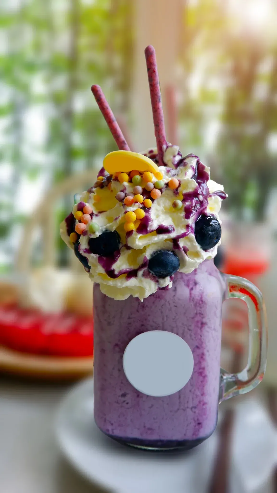 Batido morado en frasco de vidrio, cubierto con crema batida, bayas, chispas y palitos de oblea.