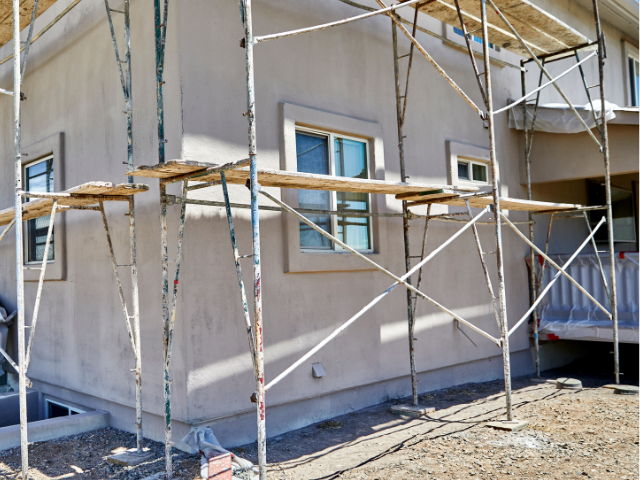 Extérieur du bâtiment en construction ; un échafaudage entoure les murs en stuc avec des fenêtres.