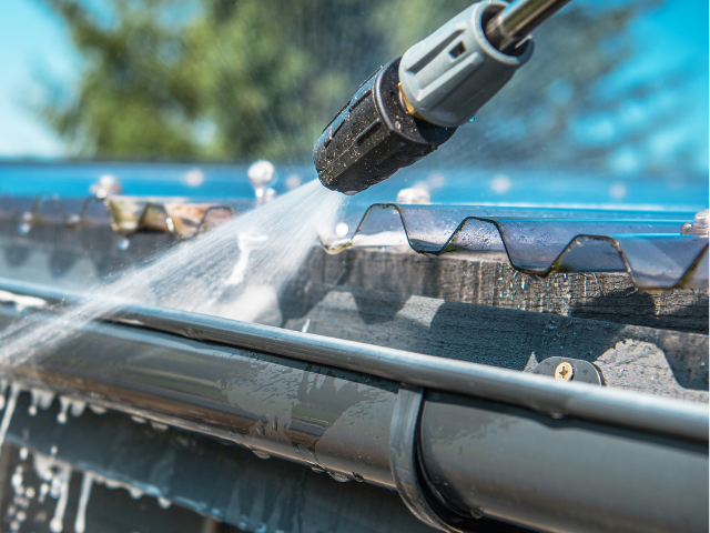 Nettoyeur haute pression pulvérisant de l'eau dans une gouttière noire, nettoyant les débris.