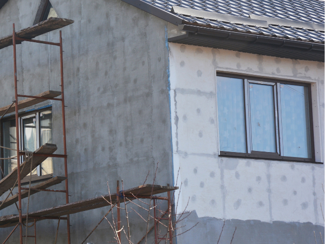 Mur extérieur de la maison en construction avec échafaudage. Enduit gris et fenêtres visibles.