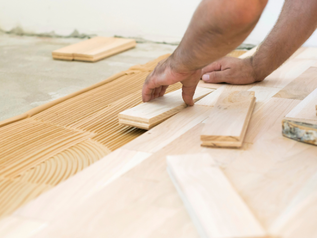 Personne installant un parquet en bois dur ; mains plaçant des planches de bois sur de la colle.