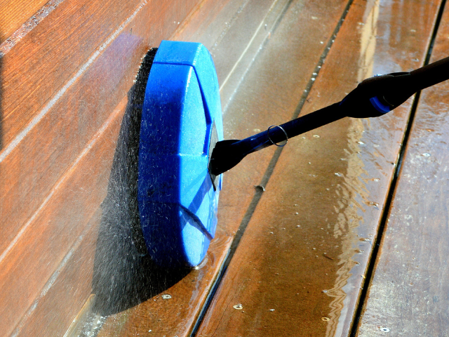 Tête de nettoyeur haute pression bleue nettoyant une terrasse en bois.