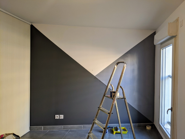 Chambre avec dessin de peinture géométrique en blanc et gris, échelle devant le mur, fenêtre à droite.
